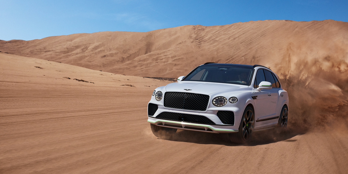 Bentley Katowice Bentley Bentayga Speed SUV front three quarter in Snow Quarts Pearlescent by Mulliner white paint driving dynamically through the desert