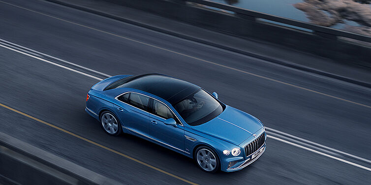 Bentley Katowice New Bentley Flying Spur Azure sedan in Light windsor blue paint by Mulliner, with 22 inch Azure wheels seen from overhead driving dynamically on a country road