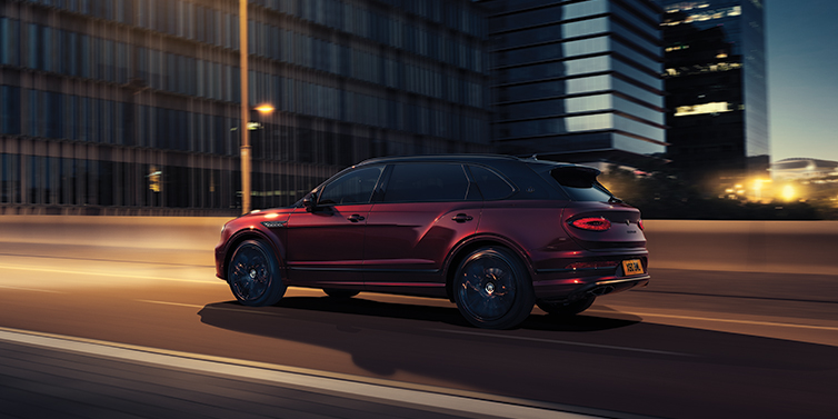 Bentley Katowice Bentley Bentayga Extended Wheelbase Mulliner SUV in Cricket Ball red paint driving dynamically in city at night