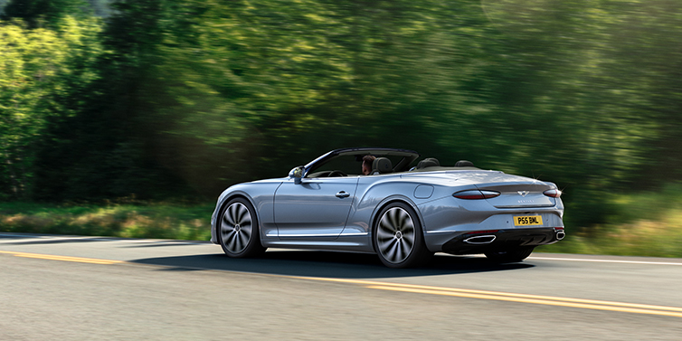 Bentley Katowice New Bentley Continental GTC convertible side view in Silverlake paint with 22 inch ten spoke wheels driving dynamically on a country road